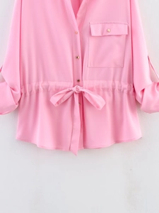Detail of pink satin shirt featuring gold buttons, drawstring waist and chest pocket