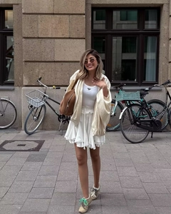 Dettaglio di un top senza maniche bianco con logo e giacca beige a maniche lunghe