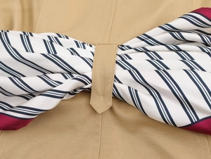Detail of khaki trench jacket featuring a striped scarf tied in a bow on the back
