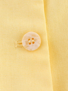 Detailansicht des Marmorknopfs und feiner Nähte am hellgelben Weste-Shorts-Set