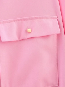 Detail of pink fabric flap pocket with a polished gold button on a women's shirt