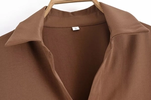 Détail du col d'une chemise marron café avec étiquette taille S sur cintre en bois