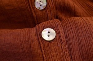 Detail von karamellfarbenem Knitterstoff und schillernden Muschelknöpfen am Hemd