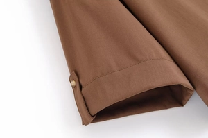 Gros plan sur le tissu marron lisse et le bouton rond naturel sur l'ourlet de la manche
