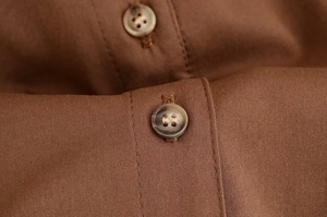 Gros plan d'un bouton en résine sur un tissu en sergé marron avec coutures précises