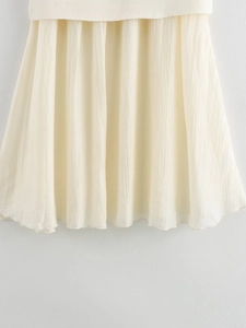 Close-up of knit fabric texture and pleated chiffon skirt hem in creamy white