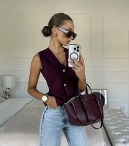 Détail du gilet en tricot bordeaux à boutons dorés et sac fourre-tout en cuir assorti