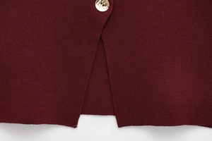 Detailed macro view of the slit hem and marble texture button on burgundy knit vest