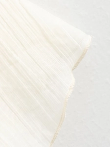 Detail of white pleated knit fabric with fine vertical texture and professional overlock stitching