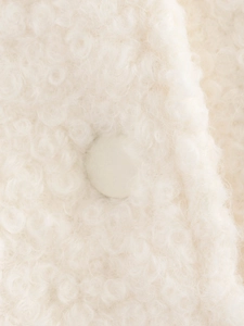 Gros plan sur la texture pelucheuse blanche et le bouton en tissu assorti de la veste
