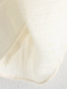 Detailed macro view of the cream-colored knit fabric with natural fringe edges and texture
