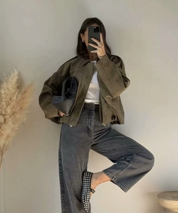 Detail of army green suede bomber jacket styled with grey high-waist jeans and accessories