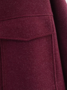 Detailed macro view of burgundy wool coat with flap pocket and decorative stitching
