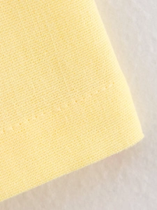 Detailansicht des gelben Baumwollstoffs mit feinen Nähten und Textilstruktur