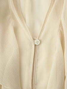 Detail van de elegante V-hals met knoop en ruches textuur op een gebroken witte blouse