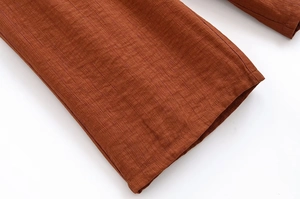 Detailansicht der plissierten Stoffstruktur und Saumnaht der braunen Hose mit weitem Bein