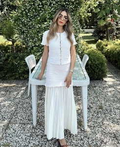 Détail du haut en tweed blanc avec boutons perlés et jupe plissée dans un jardin fleuri