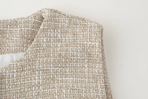 Dettaglio ravvicinato del gilet in tweed beige con trama intrecciata e fodera in seta