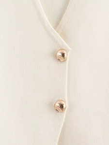 Close-up of cream knit fabric featuring decorative gold spherical metal buttons and texture