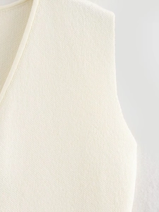 Gros plan du gilet en maille crème montrant le col en V et la texture des mailles lisses