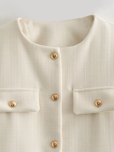 Dettaglio della giacca in tweed beige con bottoni dorati e trama del tessuto a vista