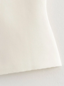 Detailed close-up of fine white knit fabric texture and smooth hemline of the top