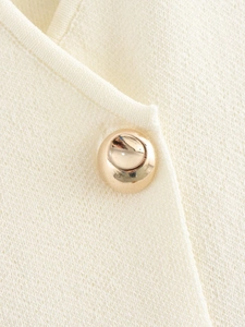 Close-up of cream knit fabric texture with a premium gold spherical button detail