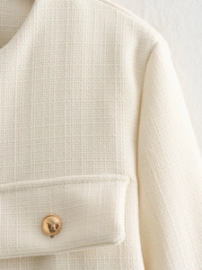 Dettaglio della giacca in tweed crema con bottoni in metallo dorato e tessuto strutturato