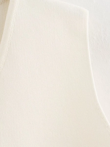 Détail macro du haut en tricot crème montrant le col en V et les coutures soignées