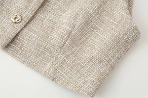 Vista dettagliata della trama del tessuto tweed beige con bottone dorato decorativo