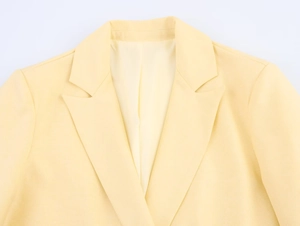 Detail of pale yellow blazer with notch lapel and fine woven texture on white background