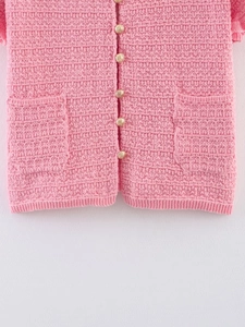 Détail d'un gilet en maille rose avec boutons vintage dorés et poches texturées