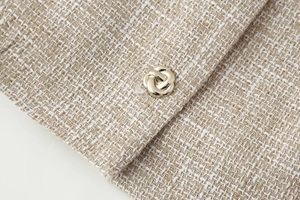 Dettaglio del tessuto in tweed beige con un bottone decorativo in metallo dorato