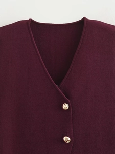 Détail d'un gilet en tricot bordeaux avec col en V et boutons métalliques dorés