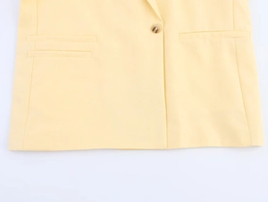 Detail view of light yellow blazer featuring amber button closure and welt pockets