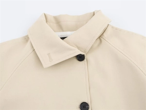 Detail of lapel collar and shoulder seam on a beige trench coat with black buttons