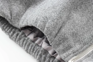 Detail of grey bomber jacket showing wool-blend texture with silver zipper and ribbed cuff