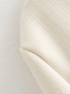 Dettaglio macro del tessuto tweed beige con trama a trama fitta e cuciture della giacca