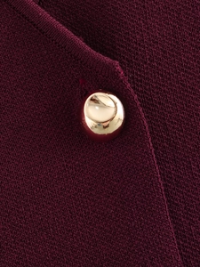 Vue macro de la maille bordeaux avec détail d'un bouton métallique doré poli brillant