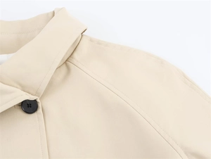 Detailed macro view of the beige trench coat lapel featuring a black resin button