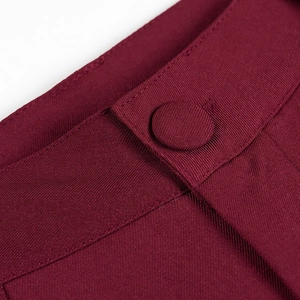 Macro view of burgundy suit trousers featuring fabric covered buttons and twill texture