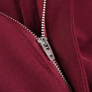 Macro shot of silver metal zipper on burgundy twill fabric showing detailed craftsmanship