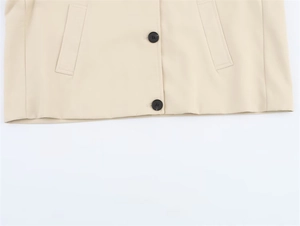 Detail view of beige trench coat hem featuring two black buttons and symmetrical side pockets