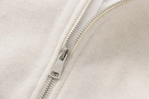 Close-up of silver metal zipper on soft cream-colored fleece bomber jacket fabric