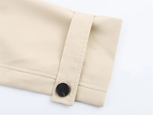 Close-up of beige trench coat sleeve detail with black button and woven strap