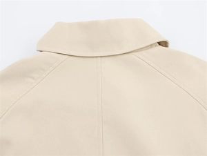 Detail view of beige trench coat featuring classic lapels and precise raglan sleeve stitching