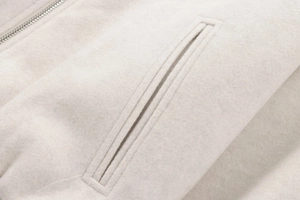 Macro shot of single-lip pocket and metal zipper on light beige wool-like bomber jacket