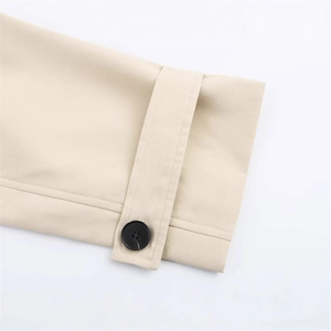 Close-up of beige short trench coat cuff with adjustable strap and black button detail