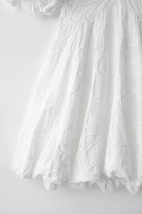 Close-up of white summer dress featuring 3D floral embossed texture and puffy sleeves