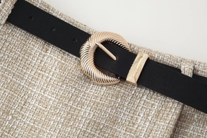 Dettaglio fibbia ovale dorata con trama radiale su cintura nera e tessuto tweed